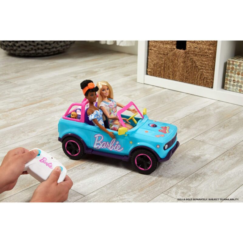 Child using the remote control to drive the Hot Wheels RC Barbie SUV with Barbie dolls inside on a living room floor.